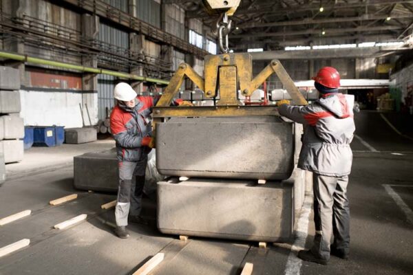 Full length portrait of two factory workers moving loads while using crane in workshop, copy space